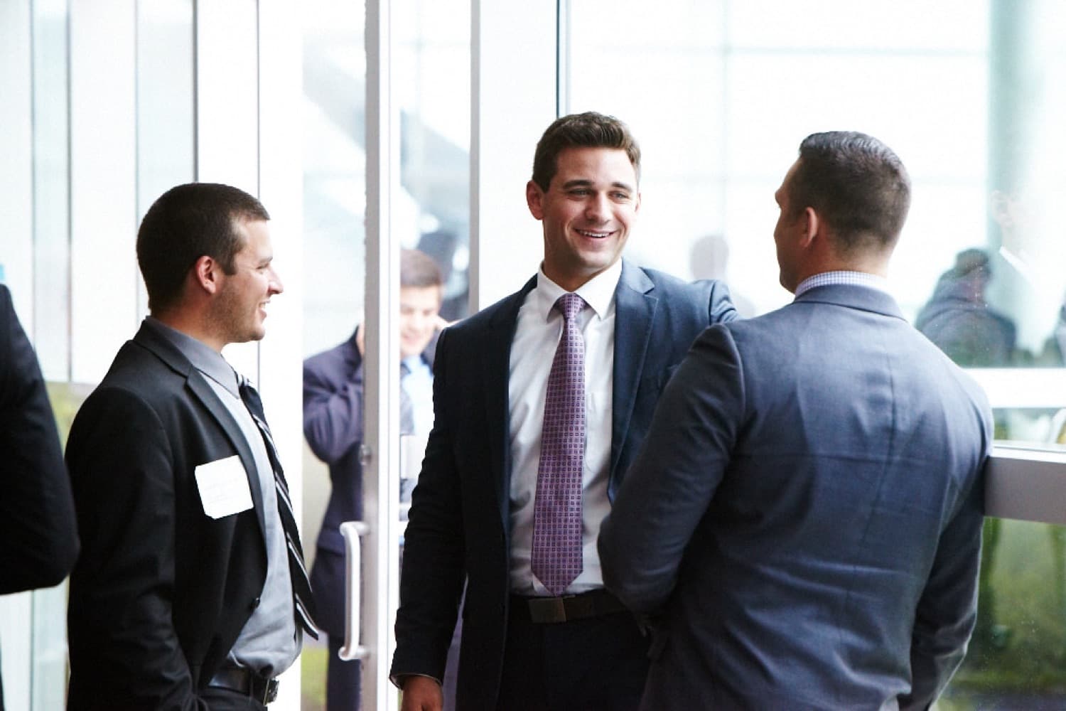 Three professionals talking and smiling in a bright, modern glass-walled office