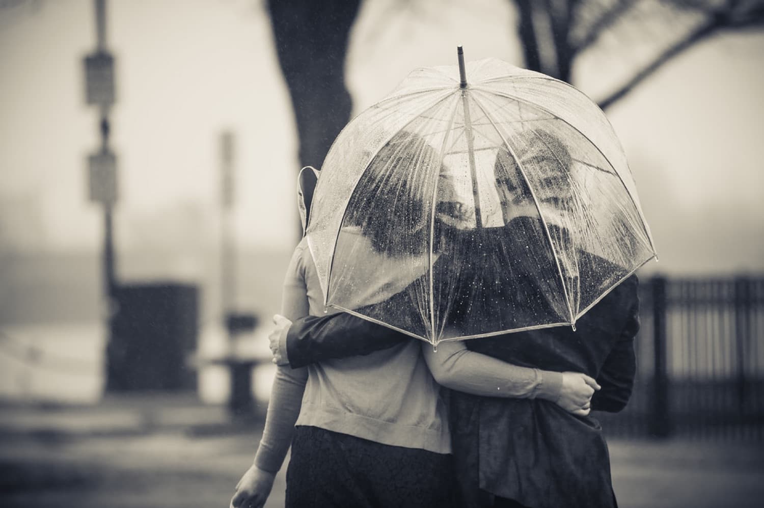 Couple sheltering under a clear umbrella in the rain