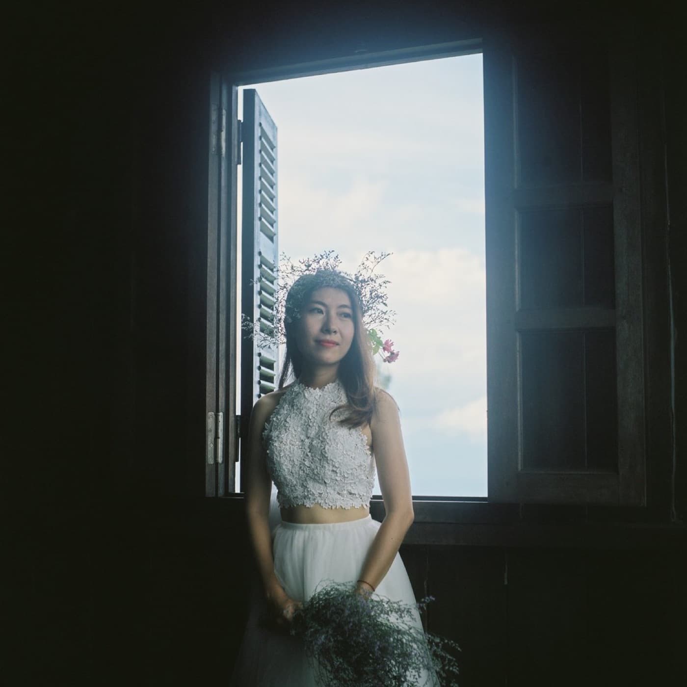 Bride in soft window light holding wildflowers